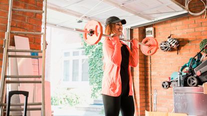 Smiling woman exercising with a barbell in a garage