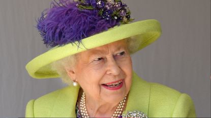 Queen Elizabeth wearing a lime green coat and hat with purple feathers smiling and looking to the right