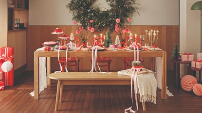 A dining room decorated for Christmas with a long rectangular dining table, a dining bench and three red chairs