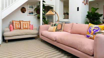 A living room with a large pink sofa with playful scatter cushions, a beige loveseat and a striped rug