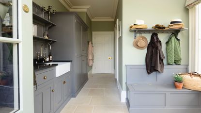 mudroom with bench storage seating and shelf above, laundry room on the left, stone floor, gray cabinetry