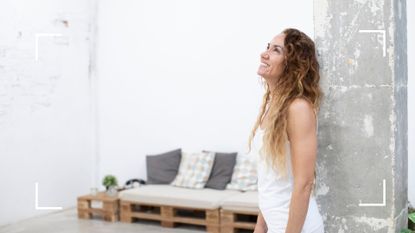 Woman smiling and leaning against concrete wall in Pilates studio, representing wall Pilates