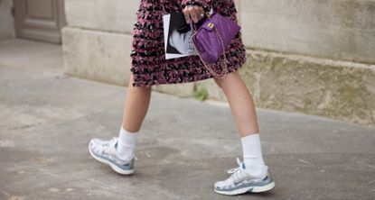 a woman walking while wearing a tweed skirt and a quilted chanel bag with sneakers