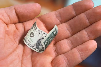 A man&#039;s hand holds a tiny US Dollar bill.