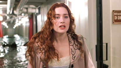 Kate Winslet standing in a flooded corridor in a still from the movie Titanic, her character has long red curly hair and she is wearing a tan coat with embroidered detailing on the collar