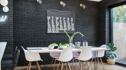 Black brick wall with calendar and wooden table with dining chairs