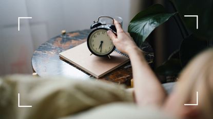 Woman&#039;s arm reaching out to turn off alarm clock away from the bed, one of the ways to learn how to wake up early in the morning in winter