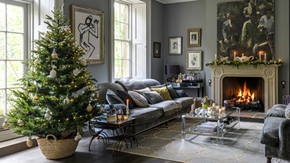 A living room decorated for Christmas with a large Christmas tree and a lit fireplace adorned with a Christmas garland