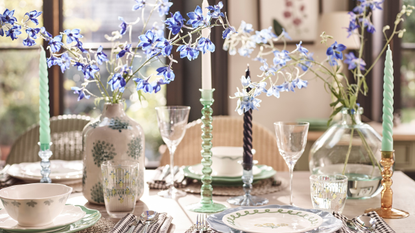 floral crockery on a dining table. There is a vase of blue flowers and blue candle holders.