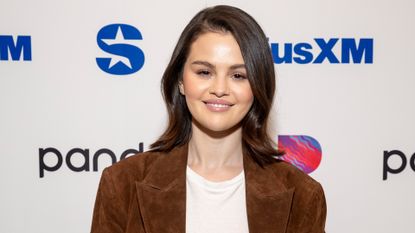 Selena Gomez wearing a suede trench coat and a white T-shirt on a red carpet