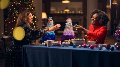 Kirstie Allsopp in a dark dress in front of a Christmas tree