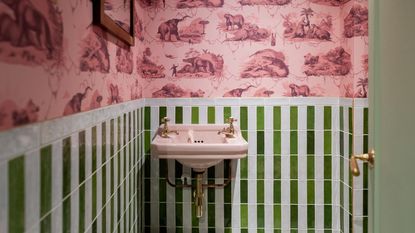 pink and green bathroom with pink wallpaper, green and white wall tiles, pink basin, gold hardware