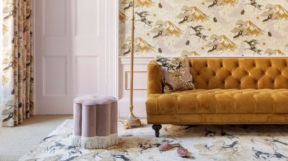 A bright living room, with pale pink accents, statement wallpaper and curtains with matching rug, velvet ochre sofa and pink pouffe