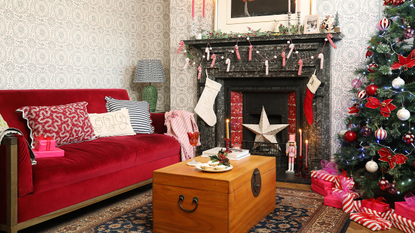 &#039;90s styled sitting room with red Christmas decorations. There is a cosy blue and orange rug, a red sofa and vintage wallpaper.