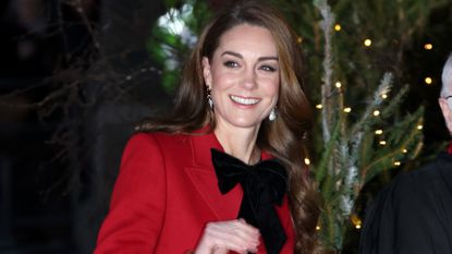 Princess Kate wears a red coat with a black bow fastened at the collar for her annual Christmas carol service at Westminster abbey on Dec. 6