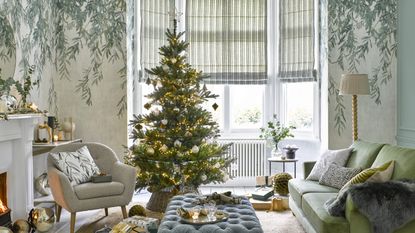 A living room with a botanical wallpaper decorated for Christmas with a fully decorated Christmas tree with lights, ornaments, a tree skirt and a topper