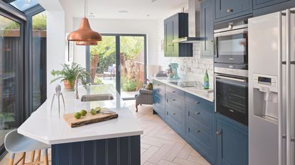 Kitchen in side return extension with dark blue units and light worktops and copper pendant over island