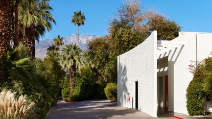 A man wearing a jacket stands in front of the entrance to Parker Palm Springs on a sunny day