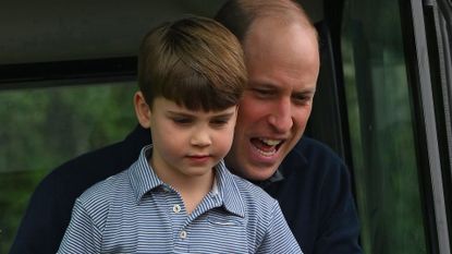 Prince William sits behind son Prince Louis and seems to be shouting while Louis looks more pensive and wears a blue and white striped polo shirt