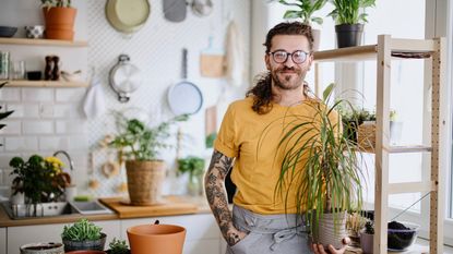 A smiling man with tattoos holds a potted dracaena