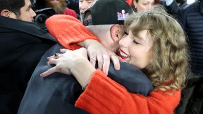 Taylor Swift hugs travis kelce at the 2024 AFC championship wearing a red sweater and pink manicure