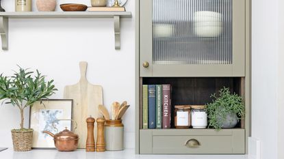 Kitchen with light green painted kitchen cabinetry and open shelving, decorated with cookbooks, crockery, and spices