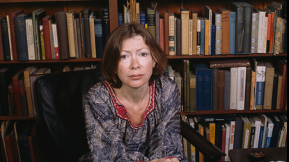 Joan Didion sitting in front of a bookshelf 