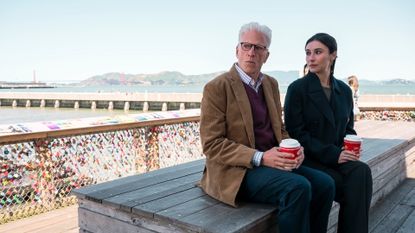 Ted Danson as Charles and Lilah Richcreek Estrada as Julie, holding take-out coffees while sitting on a wooden bench in front of the love locks, with San Francisco&#039;s Golden Gate Bridge in the background, in episode 101 of &#039;A Man on the Inside.&#039;