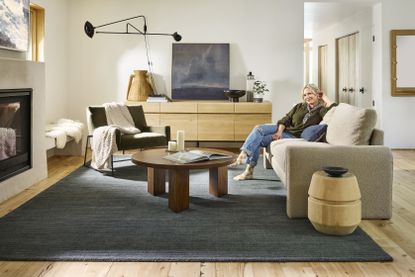 Emily Henderson sitting on an off-white couch in a modern living room that has a deep blue rug