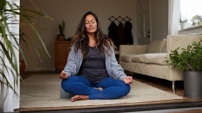 Woman practising pelvic floor yoga at home, with view of woman through open doors in back garden