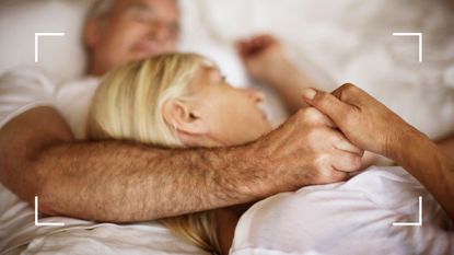 Man and woman lying in bed together embracing in white sheets, representing the Scandinavian sleep method