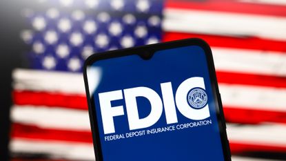 shot of the FDIC logo on a phone in front of a blurry American flag