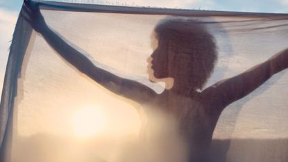 A shadow of a woman holding up a sheet to the sunlight