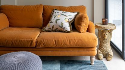 A living room with an orange velvet 3-seater sofa and a bear-shaped side table