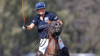 Zara Tindall wearing a blue jersey and helmet riding a horse and carrying a polo mallet