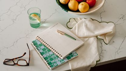 marble countertop with notebooks and pen, fruit bowl, glass of water, glasses, napkin