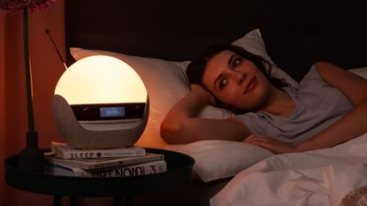 Best sunrise alarm clocks: Lumie alarm clock on a bedside table with woman slowly waking up 