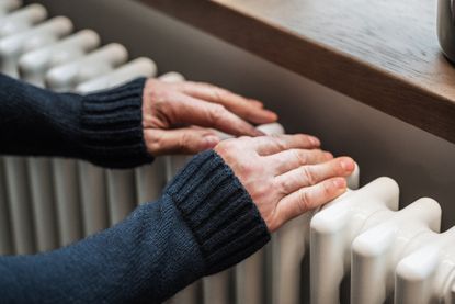 Elderly man warms his hands on the radiator