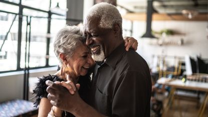 An older couple smile and dance together in a dance hall.