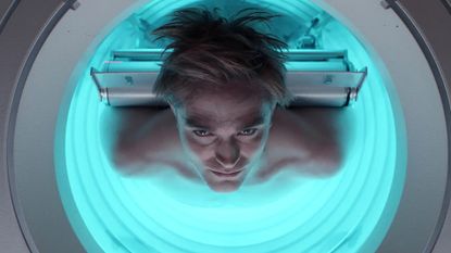 A man (Robert Pattinson) is strapped by his back to a circular machine with a neon glow on the inside, in &#039;Mickey 17.&#039;