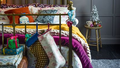 a bed with colourful bedding and bedspreads with fairy lights and a Christmas stocking at the end of the bed