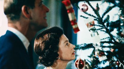 Queen Elizabeth and Prince Philip looking at a tree with red ornaments