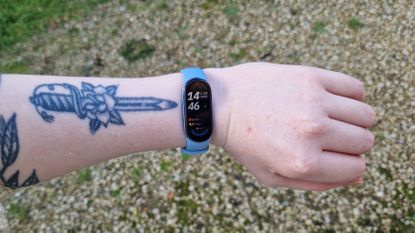 Forearm and wrist with blue fitness tracker on it. The time on the tracker reads 14:46