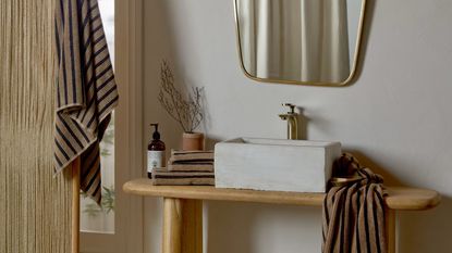 bathroom with wooden vanity, concrete sink, brass taps and mirror, striped towels