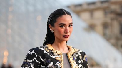 Heart Evangelista wears silver earrings, dark gray Louis Vuitton cropped top, shiny dark green Louis Vuitton leather mini skirt, black dark gray white gold pattern embroidered Louis Vuitton jacket, gold bracelets, shiny black Louis Vuitton leather bag, outside Louis Vuitton, during the Paris Fashion Week Spring/Summer 2025 on October 1, 2024 in Paris, France