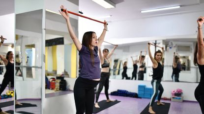 women in a studio setting with mirrors all around doing mobility moves holding resistance bands overhead 