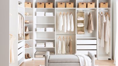 A cozy, organized bedroom with white walls and a closet, featuring clothes hung up in neat fashion, plus organizational baskets