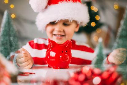 Young child in a Santa hat keeps a piggy Bank and sits in the kitchen with a decor for Christmas.