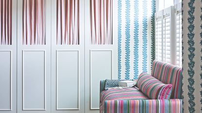 A bedroom covered in a striped wallpaper with a striped sofa and a white wardrobe with pink fabric inserts