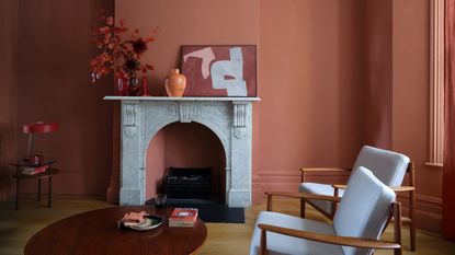 terracotta living room, color drenched walls, window and skirting, hardwood floor, marble fire surround, artwork, round coffee table, two wood upholstered armchairs, vases, side table, Farrow &amp; Ball 